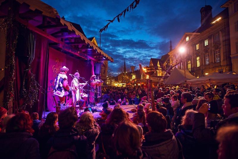 Menschenmenge genie&szlig;t eine Auff&uuml;hrung auf dem Esslinger Mittelaltermarkt & Weihnachtsmarkt bei Abendd&auml;mmerung. St&auml;nde und Lichter im Hintergrund., &copy; Esslinger Markt & Event GmbH (EME)