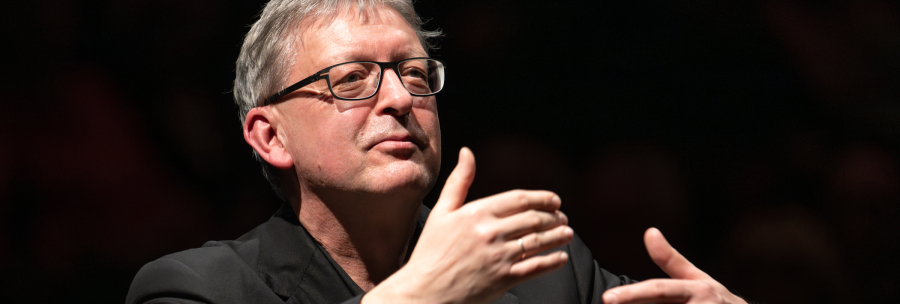 A man with glasses conducts with expressive gestures in front of a dark background., &copy; Holger Schneider