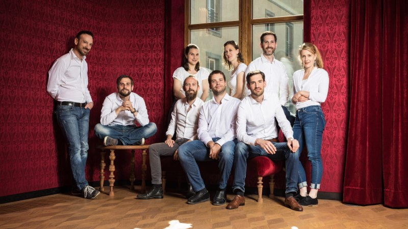 Neun Personen in weißer Kleidung posieren in einem stilvollen Raum mit roten Wänden und einem großen Fenster. Sie wirken entspannt und freundlich., © Voces Suaves Neun Personen in weißer Kleidung posieren in einem stilvollen Raum mit roten Wänden und einem großen Fenster. Sie wirken entspannt und freundlich., © Voces Suaves