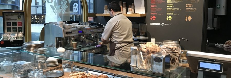 A barista in a café prepares coffee. In front of him are pastries, a coffee machine and packets of tea., © Old Bridge, Stuttgart