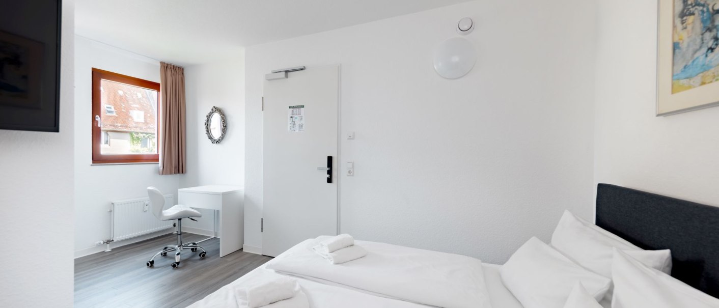 Bright double room with two beds, a desk and chair. A window with curtain and a wall mirror are visible., © Hotel Olgaeck Bright double room with two beds, a desk and chair. A window with curtain and a wall mirror are visible., © Hotel Olgaeck