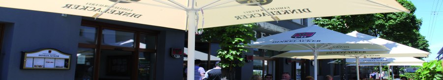 Outdoor area of the Dinkelacker brewery restaurant with wooden benches and parasols. Guests sit in the shade and enjoy the weather., © © Stuttgart-Marketing GmbH (SMG)