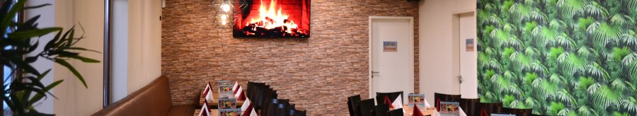 Ein langer Tisch in einer Lounge, dekoriert mit roten und wei&szlig;en Servietten. An der Wand ein Bildschirm mit Kaminfeuer, daneben eine gr&uuml;ne Tapete., &copy; Bowling & Billard Lounge