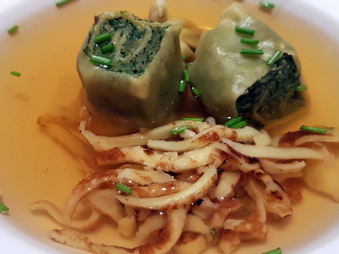 Zwei Maultaschen in klarer Brühe, garniert mit Schnittlauch und Pfannkuchenstreifen, serviert in einer weißen Schüssel., © Kultweine-Kochwelten-Kunstücke - Kochschule Sonja Lenz Zwei Maultaschen in klarer Brühe, garniert mit Schnittlauch und Pfannkuchenstreifen, serviert in einer weißen Schüssel., © Kultweine-Kochwelten-Kunstücke - Kochschule Sonja Lenz