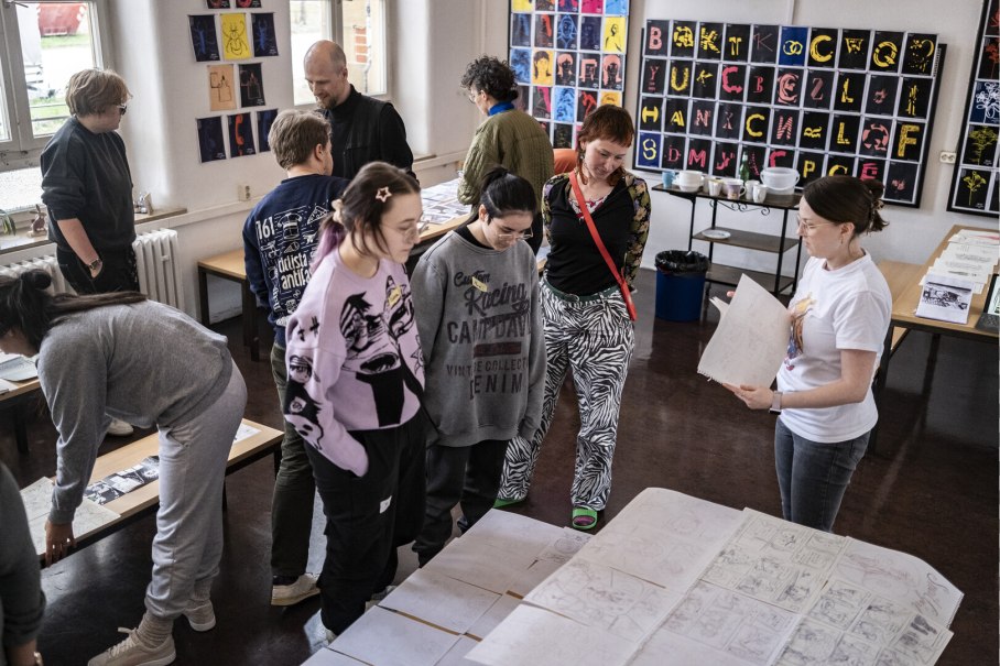 Menschen in einem Raum betrachten Zeichnungen auf Tischen. An den W&auml;nden h&auml;ngen bunte Kunstwerke. Die Atmosph&auml;re wirkt kreativ und konzentriert., &copy; Merz Akademie