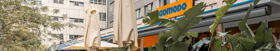 Au&szlig;enbereich eines Caf&eacute;s mit blauen St&uuml;hlen, Tischen und Pflanzen. Das Schild 'comodo' ist sichtbar. Sonnenschirme sind aufgestellt., &copy; Stuttgart Marketing GmbH, Sarah Schmid