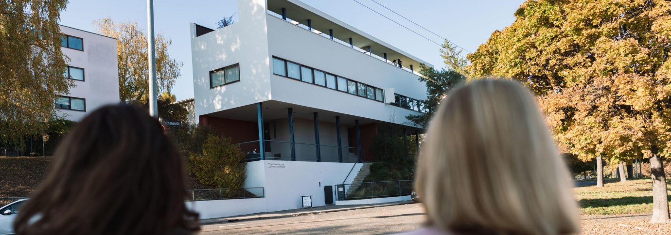 Zwei Personen betrachten das Haus Le Corbusier in der Wei&szlig;enhofsiedlung. Modernes Geb&auml;ude mit klaren Linien, umgeben von herbstlichen B&auml;umen., &copy; Stuttgart-Marketing GmbH, wpsteinheisser