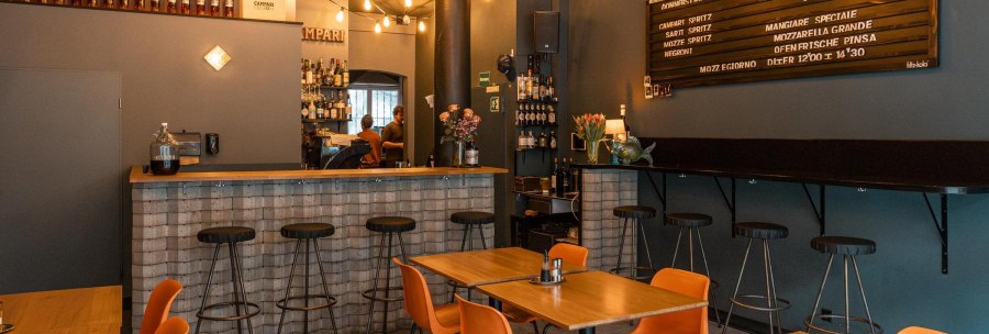 Gemütliche Bar mit Holztischen, Barhockern und einer Theke. Lichterketten und ein Menübrett schmücken die Wand., © SMG, Sarah Schmid Gemütliche Bar mit Holztischen, Barhockern und einer Theke. Lichterketten und ein Menübrett schmücken die Wand., © SMG, Sarah Schmid