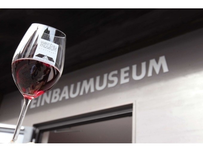 Ein Weinglas mit Rotwein wird vor dem Eingang des Weinbaumuseums in die Höhe gehalten., © Stuttgart Marketing GmbH, Thomas NIedermüller