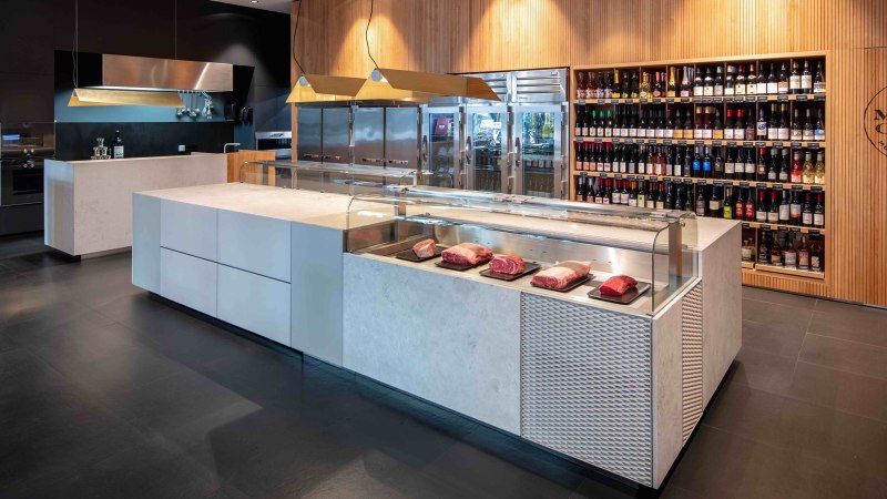 Modern meat store with a counter displaying pieces of meat. A shelf with wine bottles in the background. Wood paneling and stylish furnishings., © Meat Club, Stuttgart