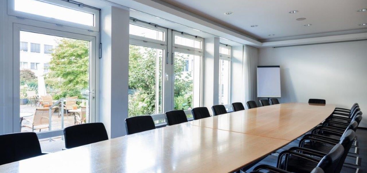 Empty meeting room with a long wooden table, black chairs and large windows overlooking a terrace with plants., © Kronen Hotel GmbH