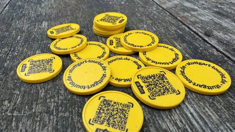 Gelbe Chips mit QR-Codes und der Aufschrift stuttgart-tourist.de liegen auf einem Holztisch verstreut., © SMG