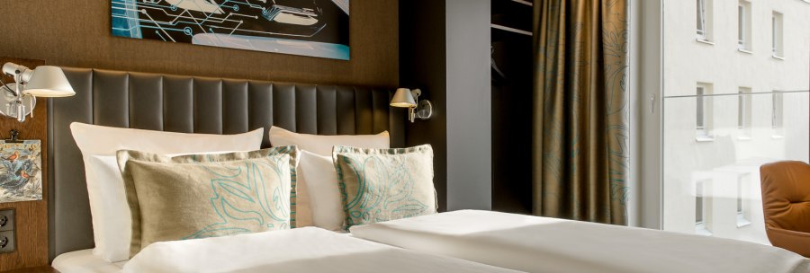 Modernes Hotelzimmer mit Doppelbett, Kunstwerk an der Wand, großen Fenstern und eleganter Einrichtung., © TOMAS Modernes Hotelzimmer mit Doppelbett, Kunstwerk an der Wand, großen Fenstern und eleganter Einrichtung., © TOMAS