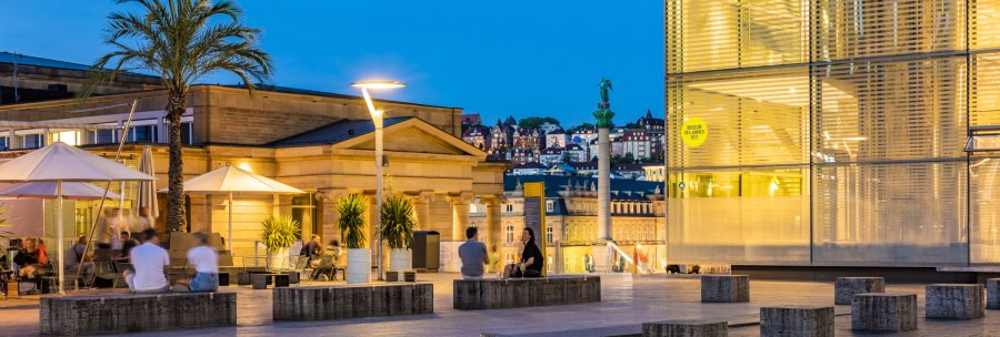 Evening atmosphere at Kleiner Schlossplatz with palm trees, people and modern architecture. Illuminated buildings and a statue can be seen in the background., &copy; SMG, Werner Dieterich