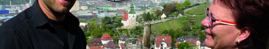 Two people toasting with wine glasses, in the background a view of the town with vineyards. Lettering "Besenwirtschaft Rauscher" and grape logo., © Besenwirtschaft Rauscher