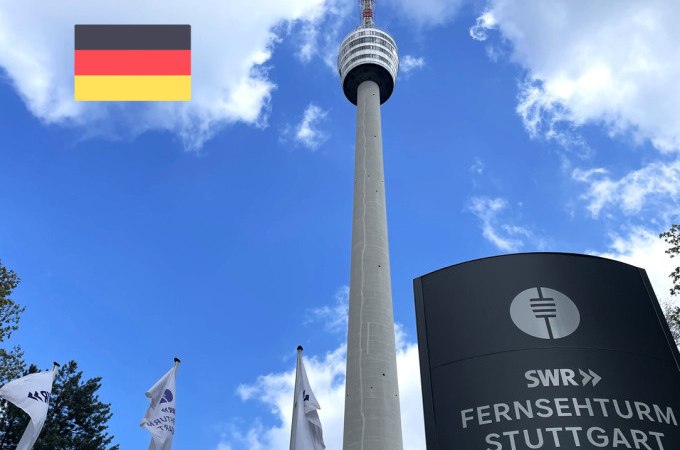 Der Fernsehturm Stuttgart ragt in den blauen Himmel, umgeben von Fahnen. Eine deutsche Flagge ist oben links im Bild zu sehen., © SWR Media Services GmbH / Fernsehturm Stuttgart Der Fernsehturm Stuttgart ragt in den blauen Himmel, umgeben von Fahnen. Eine deutsche Flagge ist oben links im Bild zu sehen., © SWR Media Services GmbH / Fernsehturm Stuttgart