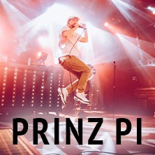 Ein Musiker springt auf der Bühne, umgeben von Lichteffekten. Im Vordergrund steht der Name 'Prinz Pi'., © links im Bild Ein Musiker springt auf der Bühne, umgeben von Lichteffekten. Im Vordergrund steht der Name 'Prinz Pi'., © links im Bild