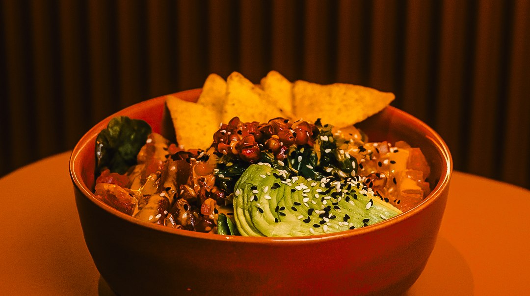 Eine Sch&uuml;ssel mit Avocado, Sesam, Gem&uuml;se und Chips steht auf einem Tisch vor einem gestreiften Hintergrund., &copy; Blackbook Studios