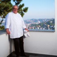 A cook in a white uniform leans against a balcony parapet. A cityscape can be seen in the background., © SMG, Jean-Claude Winkler A cook in a white uniform leans against a balcony parapet. A cityscape can be seen in the background., © SMG, Jean-Claude Winkler