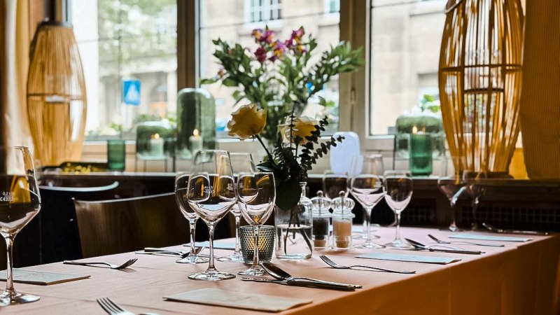 Ein elegant gedeckter Tisch in einem Café mit Weingläsern, Blumen und Kerzen, vor einem großen Fenster mit Blick nach draußen., © Cafe Stöckle FreCla, Stuttgart