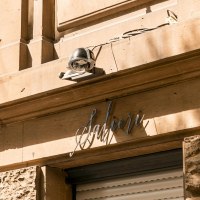 Facade of a building with the lettering 'Salieri' and a surveillance camera. The sun casts shadows on the sand-colored wall., &copy; SMG, Sarah Schmid