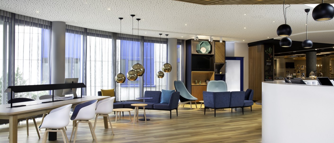 Modern lobby with wooden ceiling, blue and white furniture, decorative lamps and a reception desk., © Holiday Inn Modern lobby with wooden ceiling, blue and white furniture, decorative lamps and a reception desk., © Holiday Inn