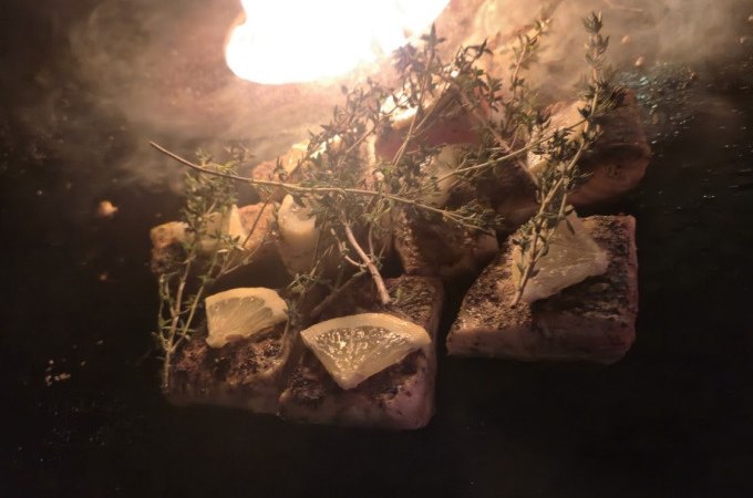 Grilled fish with lemon slices and herbs on a grill. Flames blaze in the background, creating a warm atmosphere., &copy; Cool-Tours StattReisen