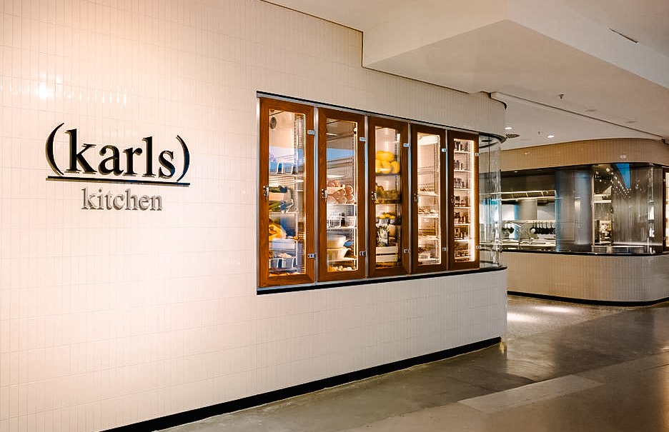 Eingang zu karls kitchen im Breuninger Stuttgart. Ein beleuchteter Schaukasten zeigt Lebensmittel. Moderne, helle Einrichtung., © Breuninger