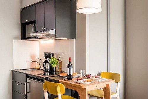 Compact kitchen with black cupboard, dining table, yellow chairs and wine bottle on the table., &copy; adagio access Stuttgart Airport Messe