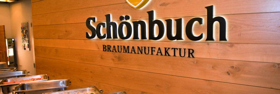 Innenansicht einer Brauerei mit Buffet. An der Holzwand steht "Schönbuch Braumanufaktur". Im Vordergrund sind Speisen in Warmhaltebehältern., © Schönbuchbrauerei, Sebastian Berger