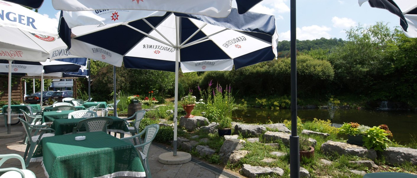 Terrace with green tables and chairs under parasols. A river and green vegetation in the background., © © H-Hotels.com Terrace with green tables and chairs under parasols. A river and green vegetation in the background., © © H-Hotels.com