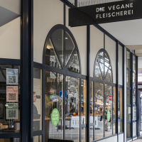 Entrance to the vegan butcher's shop in Stuttgart. The windows are large and there is a PETA Vegan Award sticker. Passers-by can be seen in the background., © Stuttgart-Marketing GmbH, Sarah Schmid Entrance to the vegan butcher's shop in Stuttgart. The windows are large and there is a PETA Vegan Award sticker. Passers-by can be seen in the background., © Stuttgart-Marketing GmbH, Sarah Schmid