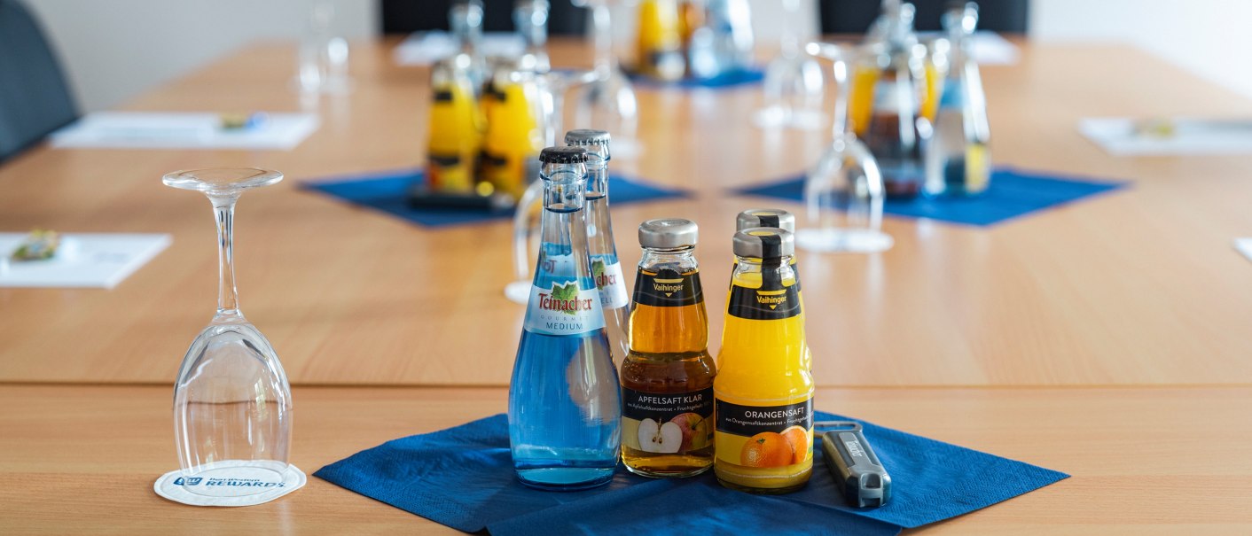 A conference table with drinks and upturned glasses. Bottles of water and juice are placed on blue napkins., © Plaza INN Stuttgart-Filderstadt A conference table with drinks and upturned glasses. Bottles of water and juice are placed on blue napkins., © Plaza INN Stuttgart-Filderstadt