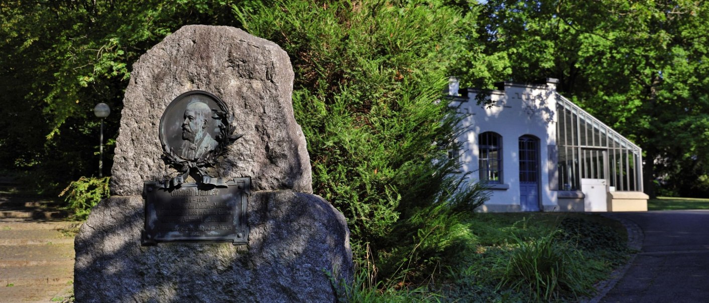 Gedenkstein für Gottlieb Daimler in einem grünen Park, rechts ein weißes Gebäude mit Glasfenstern., © Stuttgart-Marketing GmbH Achim Mende Gedenkstein für Gottlieb Daimler in einem grünen Park, rechts ein weißes Gebäude mit Glasfenstern., © Stuttgart-Marketing GmbH Achim Mende
