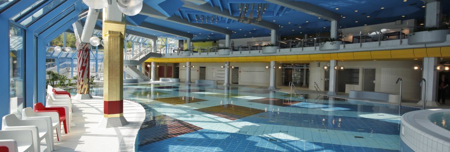 Modern swimming pool with blue ceiling, colorful tiles and white and red chairs along the pool., &copy; Stuttgarter B&auml;der