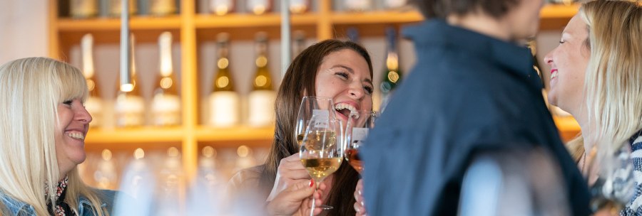 Vier Personen sto&szlig;en in einer Vinothek mit Weingl&auml;sern an und lachen. Im Hintergrund sind Weinflaschen zu sehen., &copy; Stuttgart-Marketing GmbH, Thomas Niederm&uuml;ller