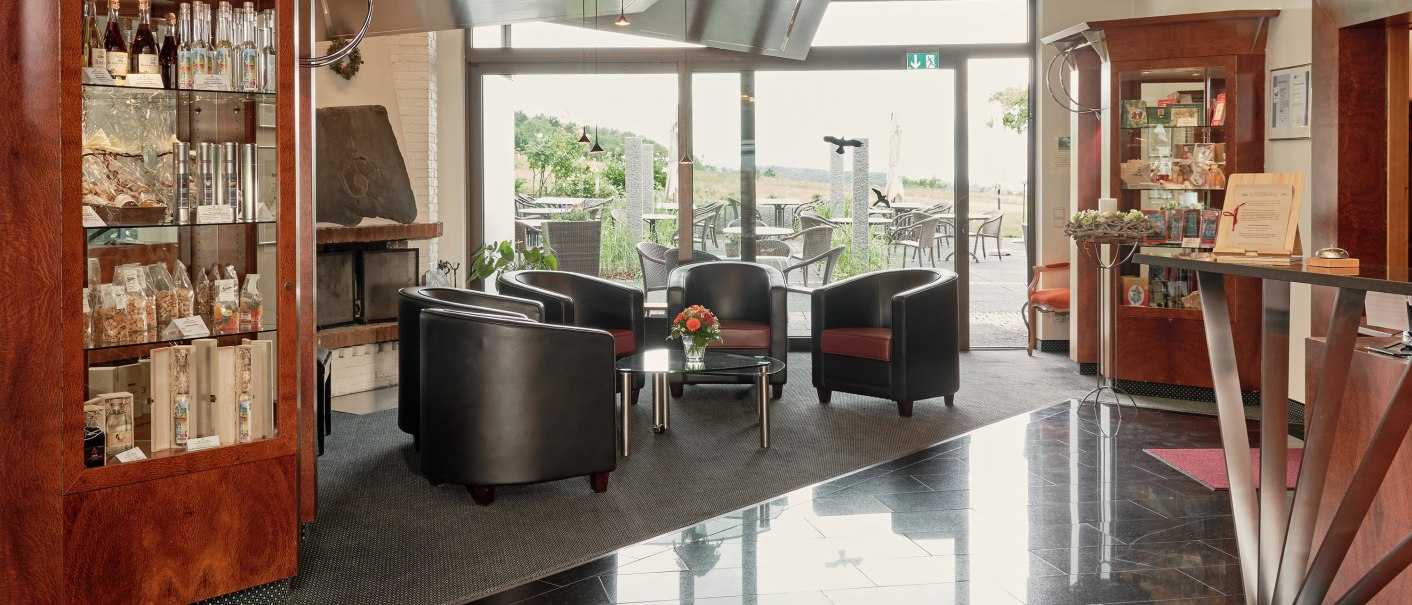 Moderner Empfangsbereich mit Ledersesseln, Glastisch, Glasvitrine und Blick auf eine Terrasse im Badhotel Restaurant Stauferland., © Badhotel Restaurant Stauferland