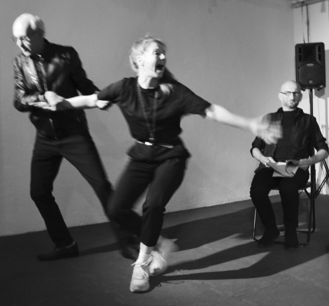 Schwarz-weiß-Foto: Eine Frau wird von einem Mann gezogen, während ein anderer Mann sitzt und zuschaut. Die Szene wirkt dynamisch und emotional., © Theater 360 Grad