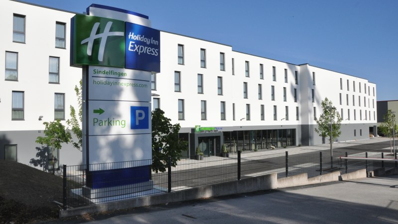 Das Holiday Inn Express in Sindelfingen zeigt eine moderne Fassade mit einem gro&szlig;en Parkplatzschild im Vordergrund. Der Himmel ist klar und blau., &copy; tristar GmbH