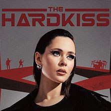 Frau mit dunklem Haar und auff&auml;lligem Make-up vor dem 'The Hardkiss'-Logo. Im Hintergrund sind Silhouetten von Bandmitgliedern zu sehen., &copy; links im Bild