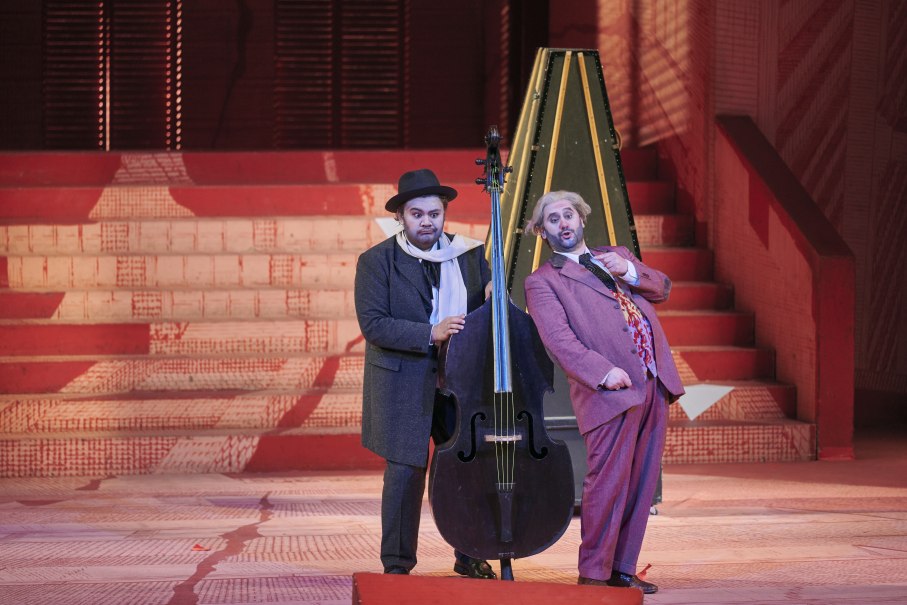 Zwei M&auml;nner in Kost&uuml;men stehen auf einer Opernb&uuml;hne. Einer h&auml;lt einen Kontrabass, der andere gestikuliert. Im Hintergrund sind rote Treppen zu sehen., &copy; Martin Sigmund