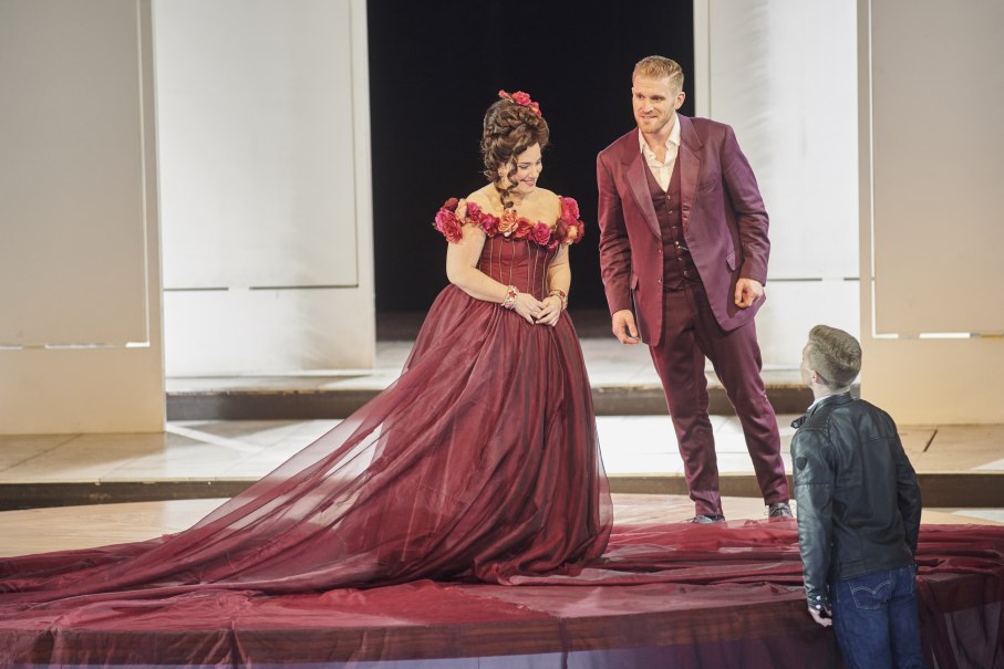 Two actors in elegant clothes on the stage of an opera performance. The woman is wearing a burgundy dress, the man a matching suit., &copy; Martin Sigmund