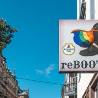 A sign with a boot and a rainbow flag, next to it the inscription 'reBOOTS'. Buildings and a tree can be seen in the background., © SMG Stuttgart Marketing GmbH - Sarah Schmid A sign with a boot and a rainbow flag, next to it the inscription 'reBOOTS'. Buildings and a tree can be seen in the background., © SMG Stuttgart Marketing GmbH - Sarah Schmid