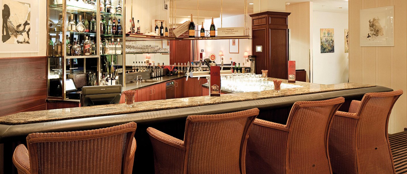 Elegante Hotelbar mit Rattanstühlen, Marmortheke und beleuchtetem Regal voller Spirituosen. Dezente Beleuchtung und stilvolle Dekoration., © Seminaris Hotel Bad Boll