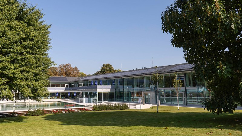 The picture shows the outdoor area of the Mineralbad Berg with a pool, surrounded by modern buildings and green trees under a clear sky., © Stuttgarter Bäder