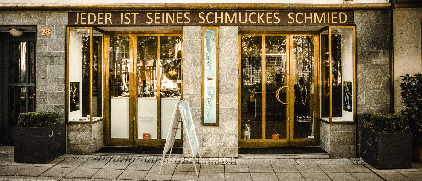 Ein Schmuckgeschäft mit der Aufschrift 'Jeder ist seines Schmuckes Schmied' über dem Eingang. Die Fassade ist aus Stein, mit großen Fenstern und einer Holztür., © Goldmond