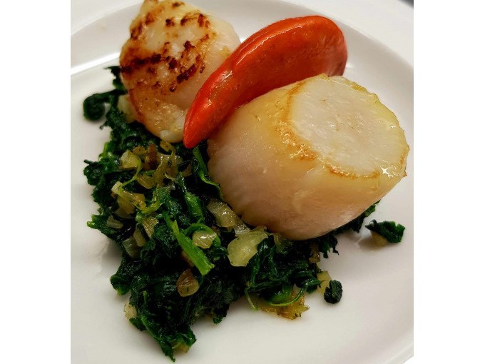 Fried scallops on a bed of spinach and onions, decorated with a red slice, served on a white plate., &copy; Kultweine-Kochwelten-Kunst&uuml;cke - Kochschule Sonja Lenz