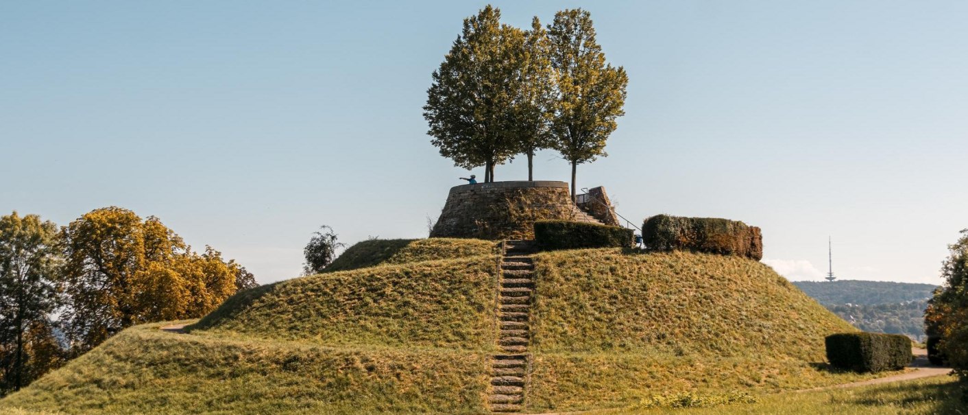 Eine grasbewachsene Erhebung mit einer Treppe führt zu einer Plattform mit Bäumen. Der Himmel ist klar und blau., © Stuttgart-Marketing GmbH, Sarah Schmid