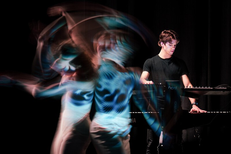 Ein Musiker spielt Keyboard, w&auml;hrend ein T&auml;nzer in dynamischer Bewegung verschwommen ist. Die Szene wirkt k&uuml;nstlerisch und energiegeladen., &copy; W&uuml;rttembergische Staatstheater Stuttgart