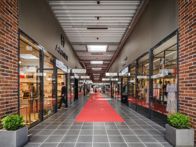 Einkaufspassage mit roten Teppichen, Geschäften wie Aigner auf beiden Seiten und Menschen beim Einkaufen., © Schlienz-Tours GmbH & Co.KG Einkaufspassage mit roten Teppichen, Geschäften wie Aigner auf beiden Seiten und Menschen beim Einkaufen., © Schlienz-Tours GmbH & Co.KG